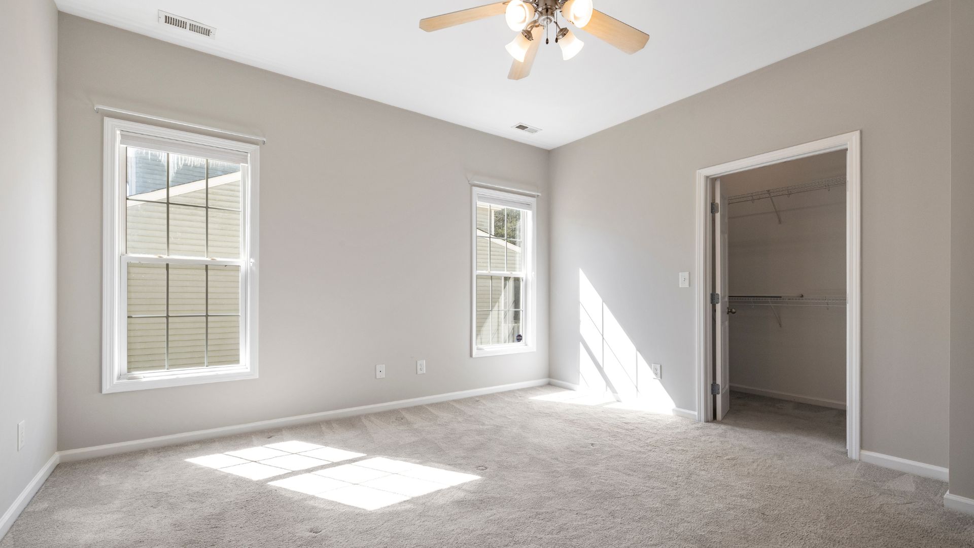 An empty room with a ceiling fan and two windows